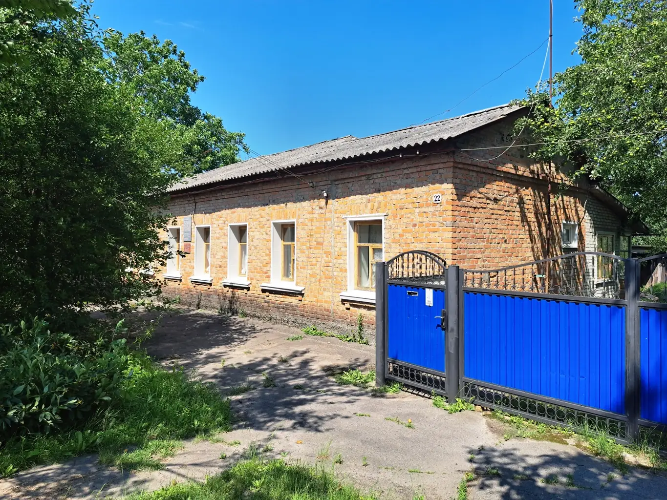 Довгий одноповерховий цегляний будинок із білими вікнами за синьою хвірткою