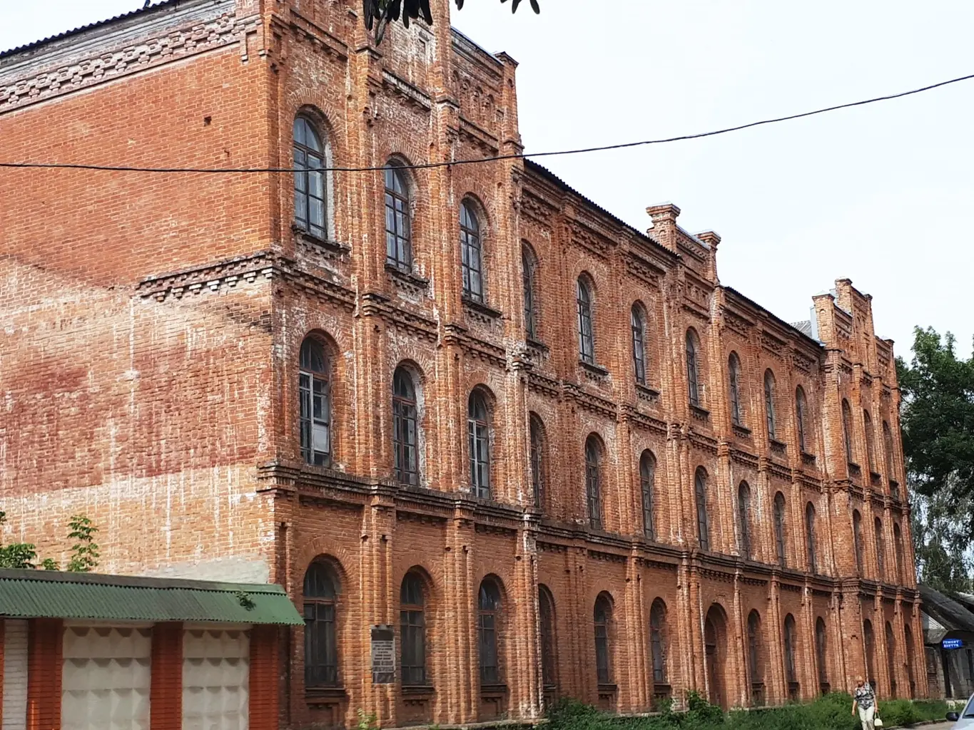 Триповерхова червона цегляна будівля з високими арковими вікнами вздовж вулиці