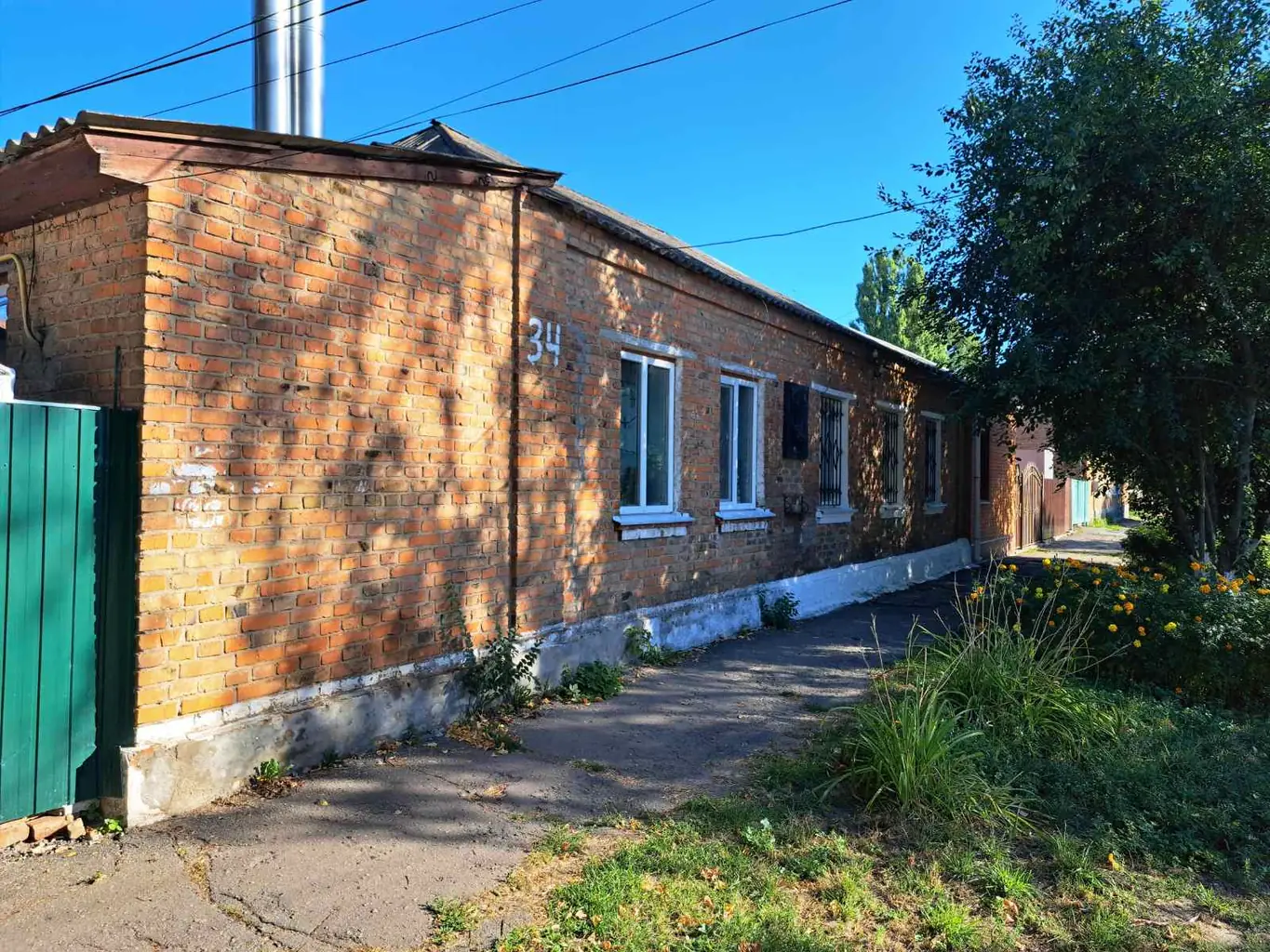Довгий одноповерховий цегляний будинок під тополями у ранковому світлі