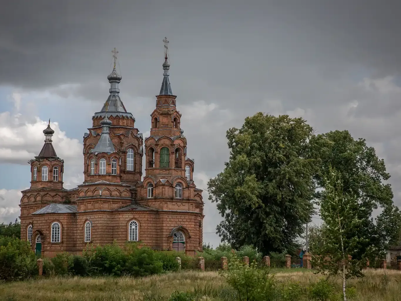 Цегляна церква з сірими банями під хмарним небом